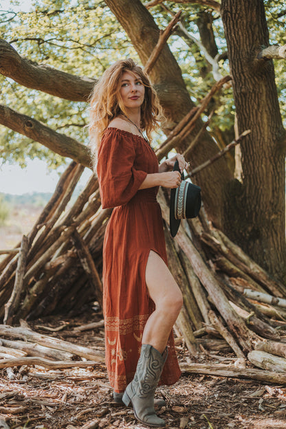 Elegante Serpentina jurk in terra cotta, met een flatterende pasvorm en speelse split – ideaal voor een chique avondje uit of zomerse brunch