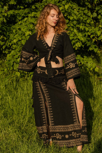 Zwarte co-ord set met een vloeiende rok en top, versierd met subtiele slangen- en maansymbolen in gouden prints, perfect voor een bohemian festivaloutfit